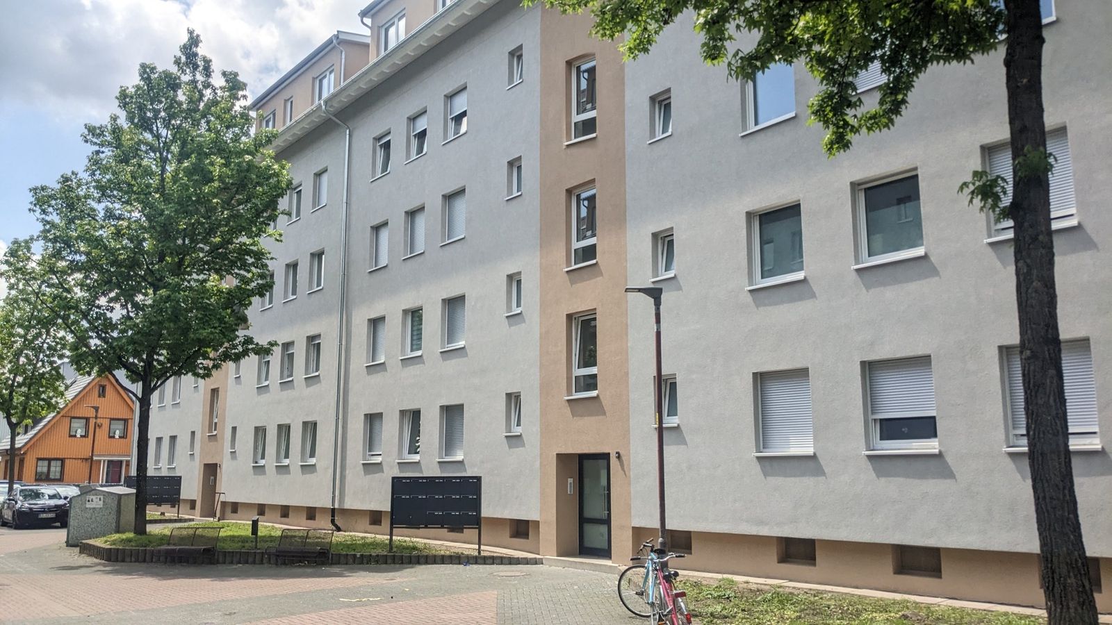 Modernisierter Bestandsbau an der Fischerstraße mit Hauseingang und Bäumen